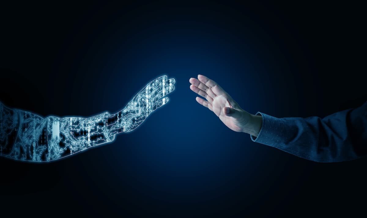 a digital futuristic hand an a human hand reach out toward one another set against a dark blue background